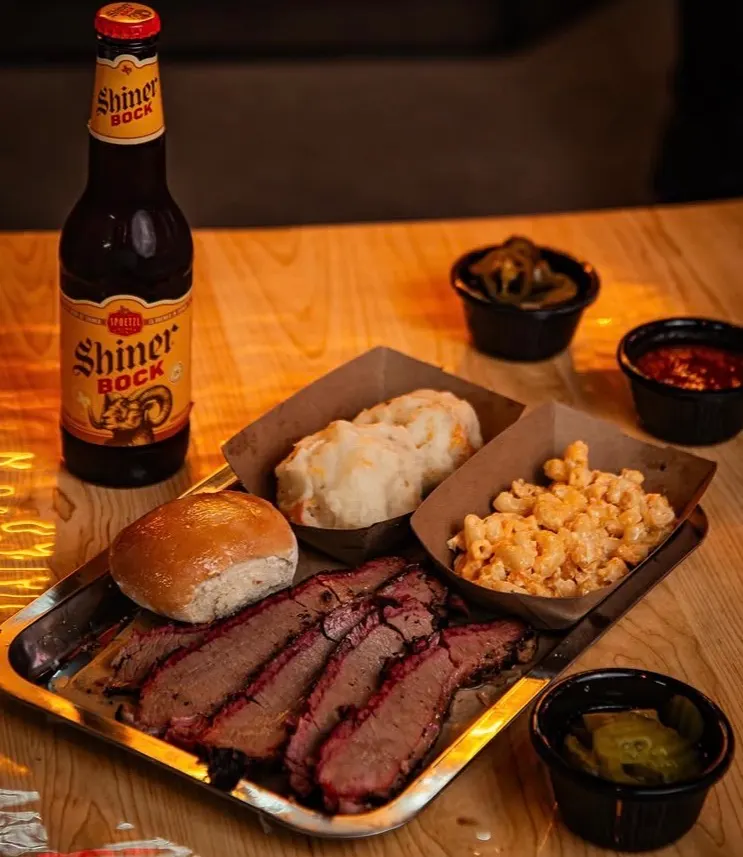 Bandeja de brisket rebanado con su corteza oscura, pan, puré, mac and cheese y una Shiner Bock