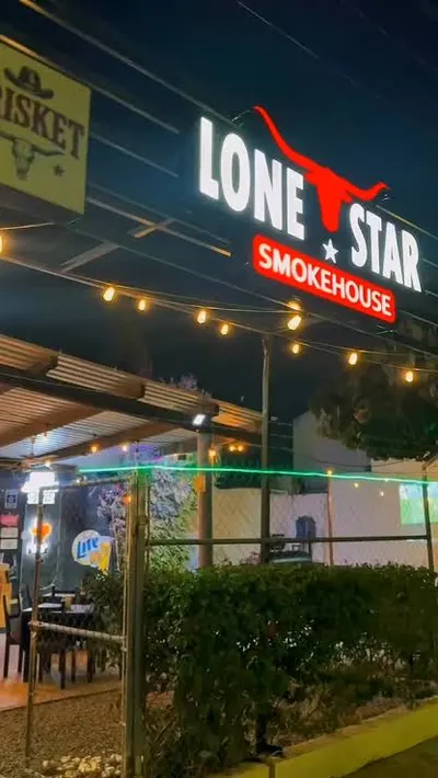 Fachada de noche con el letrero luminoso de Lone Star Smokehouse sobre el patio y sus foquitos